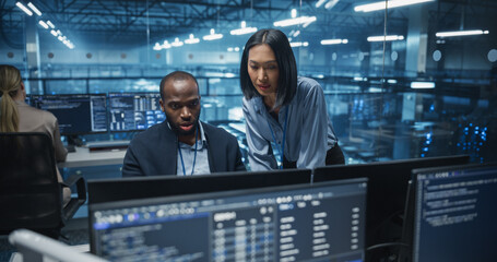 Black Male and Asian Female Engineer Collaborate on a Project in a Modern Data Center Office. Specialists Analyzing Complex Systems on Multiple Screens to Improve Cybersecurity and Performance