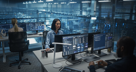 In a Data Center Office With Glass Walls, Diverse Female and Male Team Members Focus on Their Desktop Computers, Conducting Routine System Checks and Working on Network Improvements