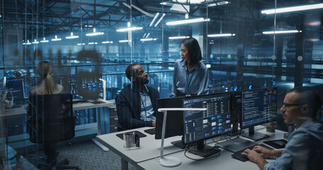 Modern Office in a Server Facility: Asian Female Data Scientist and Black Male Cybersecurity Expert Analyze Data Together on a Desktop Computer, Brainstorming New Security Solutions and Services