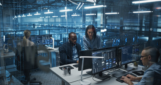 Diverse Team of Developers Working on Computers in a Modern Office in a Data Center Facility. Team Analyzing Data and Optimizing Systems. Asian Manager Having a Conversation with a Colleague - Powered by Adobe