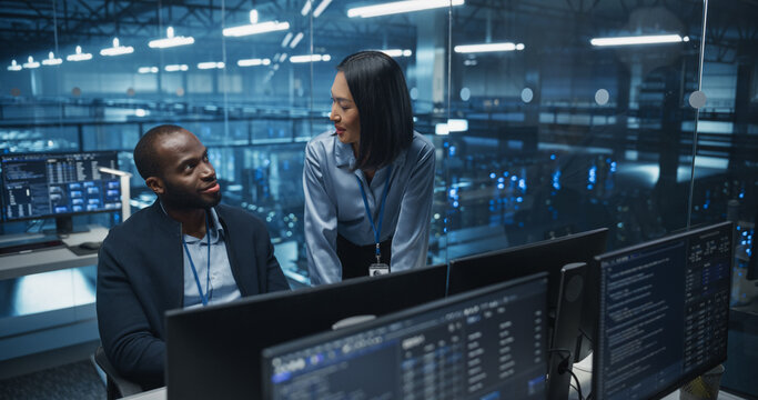 Black Male and Asian Female Engineer Collaborate on a Project in a Modern Data Center Office. Specialists Analyzing Complex Systems on Multiple Screens to Improve Cybersecurity and Performance