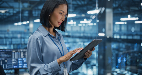 Portrait of an Asian Female Manager Studies Online Reports on Her Tablet Computer, Standing in a Modern Data Center with Server Systems. Young Woman Searching for Patterns to Improve Production