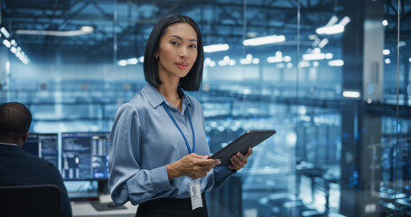 Asian Female Systems Administrator Standing in a Glass Office, Using a Tablet Computer at Work in a...