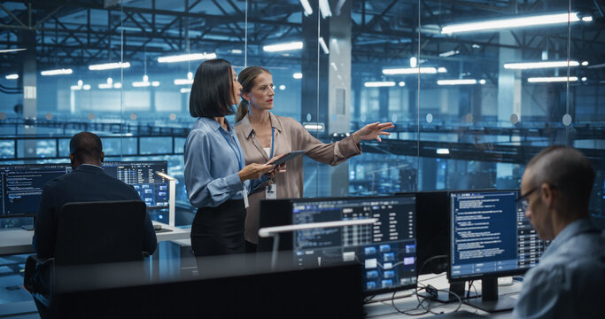 Two Diverse Female Cloud Security Engineers Work Side by Side on a Tablet Computer in a Data Center Office, Conducting a Thorough Security Audit of the Server Network Infrastructure