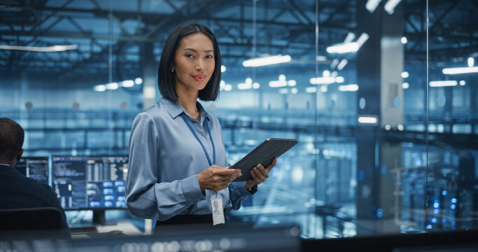 Asian Female Systems Administrator Standing in a Glass Office, Using a Tablet Computer at Work in a Technology Center. Empowering Leading Specialist Posing, Looking for Camera and Smiling
