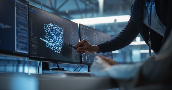 With Screen Setup Showing AI Code and Model Visualization, Female Developer Works Closely with a Black Team Leader Standing Beside Her, Discussing Improvements and Refinements to Their AI System