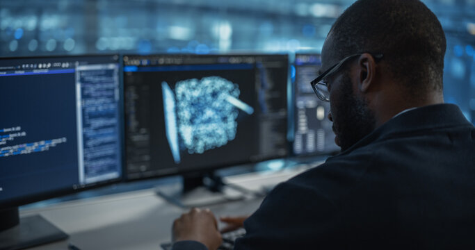 Male Software Engineer Focused on Working on a Machine Learning Model Displayed Across Three Monitors. Black Specialist Analyzing Data Outputs and Tweaking Parameters in Real Time