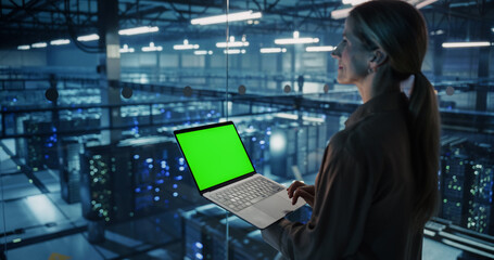 Female Information Technology Engineer Using Her Laptop Computer with Green Screen Chroma Key Display in a High-Tech Data Center, Analyzing Potential Risks to Ensure Network’s Safety and Compute Power