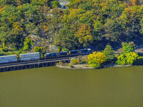 Fort Montgomery, United States - 25 October 2023: Aerial view of a train traversing the trestle bridge, contrasting against the Hudson River and vibrant foliage.