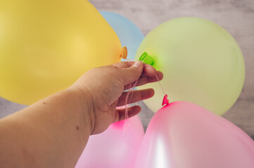 Hand holding a bunch of colorful inflated balloons in pastel shades of pink, yellow, green, and blue. Perfect for birthday parties, festive events, or holiday celebrations.