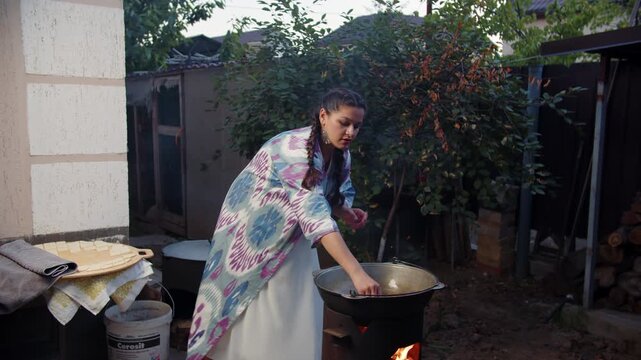 Pregnant woman frying baursak dough in kazan cauldron outdoors