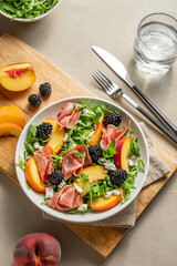 Fresh salad with peaches, arugula, feta, prosciutto and berries in a plate on a wooden board