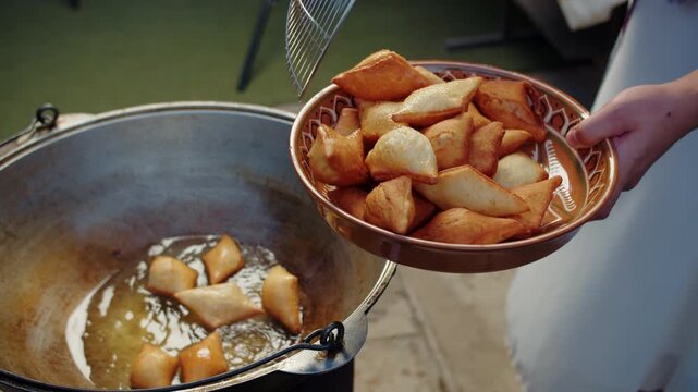 Taking golden baursak pieces from hot oil into bowl