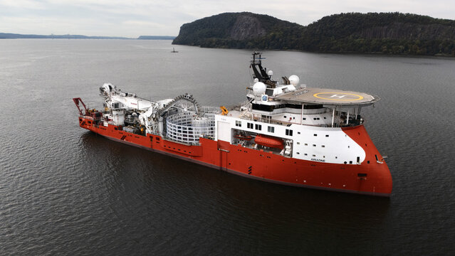Nyack, United States - 16 September 2025: Aerial view of a vibrant red and white offshore support vessel sailing on the Hudson River, framed by the lush, green shores of the Palisades cliffs.