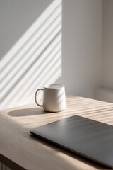 White Mug and Laptop on Light Wood Desk with Sunlit Stripes