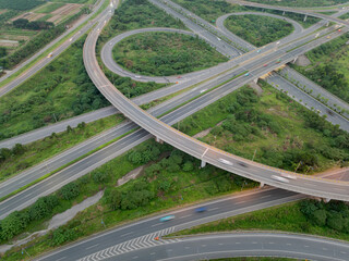 An aerial, high-angle view of a highway interchange in Hanoi during the daytime, revealing the complex, multi-level design of the intersecting roads and ramps surrounded by green trees.