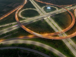 An aerial, high-angle shot of a glowing cloverleaf interchange in Hanoi at dusk, capturing the intricate curves and overpasses of the road network with subtle vehicle light trails.