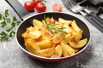 Tasty baked potatoes with rosemary in frying pan on grey textured table, closeup