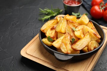 Tasty baked potatoes with parsley in frying pan on dark textured table, closeup