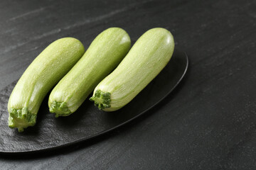 Fresh ripe zucchinis on black textured table, closeup