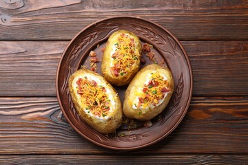 Tasty baked potatoes with sour cream, green onion, cheese and bacon on wooden table, top view