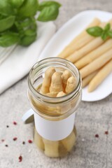 Pickled asparagus, spices and basil on light grey table, closeup
