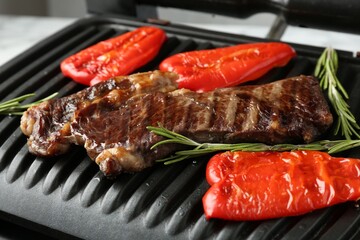 Electric grill with beef steaks, bell peppers and rosemary on white table, closeup