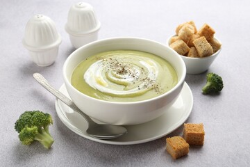 Tasty broccoli cream soup served with croutons on light grey table, closeup