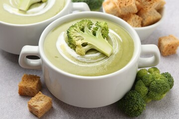 Tasty broccoli cream soup served with croutons on light grey table, closeup