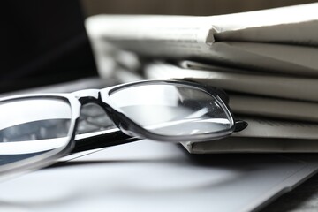 Stack of newspapers, laptop and glasses on table, closeup