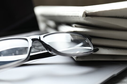 Stack of newspapers, laptop and glasses on table, closeup