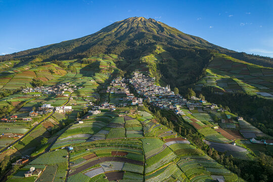 Aerial view of a majestic mountain looms over terraced fields and a quaint village nestled in its foothills, Nepal Van Java, Magelang, Jawa Tengah, Indonesia.