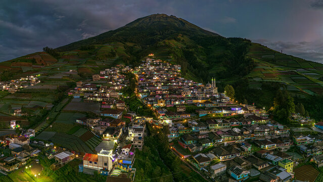 Aerial view of the illuminated village of Nepal Van Java nestled on the slopes of a verdant mountain, a tapestry of light against the twilight sky, Magelang, Jawa Tengah, Indonesia.