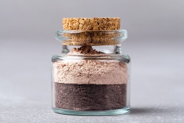 A close-up of a small glass jar containing two layers of flesh-colored powder, fitted with a cork stopper, shot in high resolution to highlight the details.