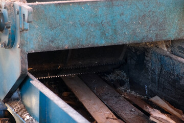 Wood scraps leftovers moving on conveyor belt to chopping machine at woodworking plant outdoors. Timber processing and woodworking industry. Wooden sawdust splinters production on saw-mill factory.