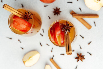 Two glasses of apple cider with cinnamon sticks, star anise, and apple slices.