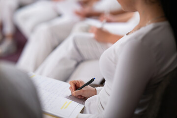 Close up of a student holding a pen and writing notes in a notebook during a professional training and education session in a wellness and therapy course