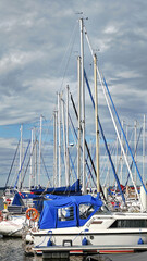 Sailing boats sit in a bay on a sunny day under a cloudy sky.