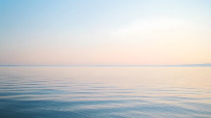 Obraz premium Serene lake vista bathed in soft, pastel hues of dawn, showcasing gentle ripples on the water's surface and a tranquil, hazy sky.