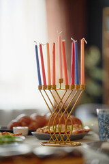 Hanukkah menorah with nine colorful candles standing on festive table, traditional Jewish holiday foods arranged in background, focus on ceremonial object during celebration