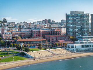 Aerial view of the Aquatic Park's sandy beach meeting the shimmering bay, contrasted by the historic brick buildings and modern high-rises, San Francisco, California, United States.