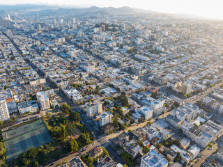 Aerial view of the sun casting long shadows across the grid-like streets and rooftops, with the distant hills adding depth to the cityscape, San Francisco, California, United States.