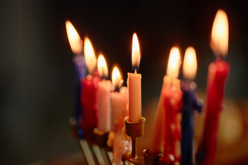 Closeup showing colorful Hanukkah candles burning in menorah, melted wax dripping down candle holders, soft focus background emphasizing traditional Jewish holiday celebration