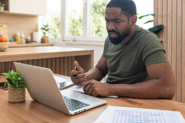 Young university student, freelancer business man, working at home on laptop computer, testing new innovative technology and online internet tools while sitting in home office.