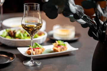 Elegant restaurant table setting with white wine, gourmet appetizers, salad, and dessert. Fine dining atmosphere with stylish plating and moody floral decor
