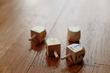 Four wooden dreidels resting on wooden surface, each displaying different Hebrew letters,...