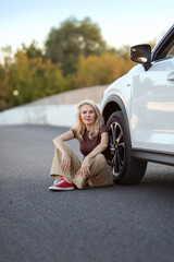 woman stands next to a light color car off a road. Travel and tourism.