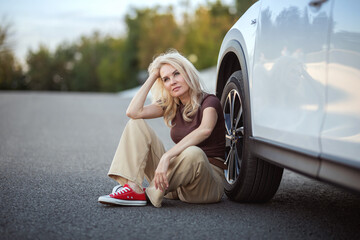 A woman is sitting on the side of the road next to a car. Travel and tourism.