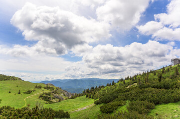 This image captures the lush green hills of Rax Austria with a backdrop of dramatic clouds illuminated by soft natural light, showcasing rich textures and undulating terrain leading