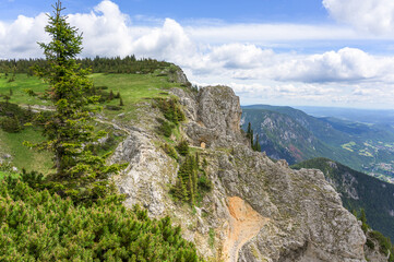A breathtaking view from Rax Mountain in Austria showcasing rocky cliffs and lush greenery under a bright blue sky with fluffy clouds, with jagged rocks contrasting with vibrant